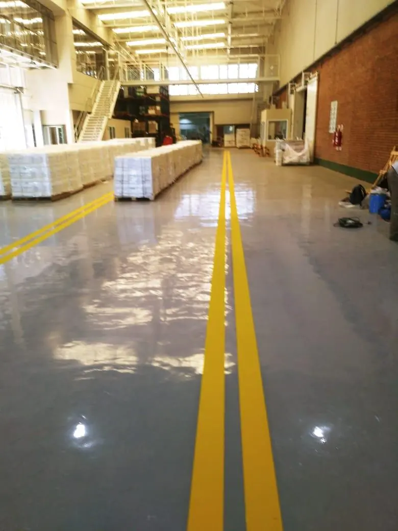 Nave industrial con piso epoxi y doble línea amarilla de demarcación que recorre el pasillo central