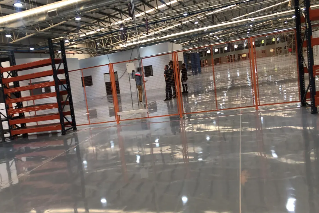 Depósito con estanterías metálicas y piso de epoxi autonivelante que refleja la estructura del techo